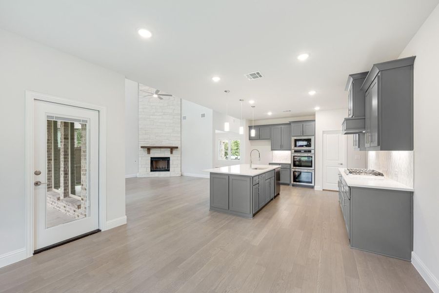 Open-concept kitchen with gray cabinets, center island, and living area with stone fireplace and hardwood floors Open-concept kitchen with gray cabinets, center island, and living area with stone fireplace and hardwood floors