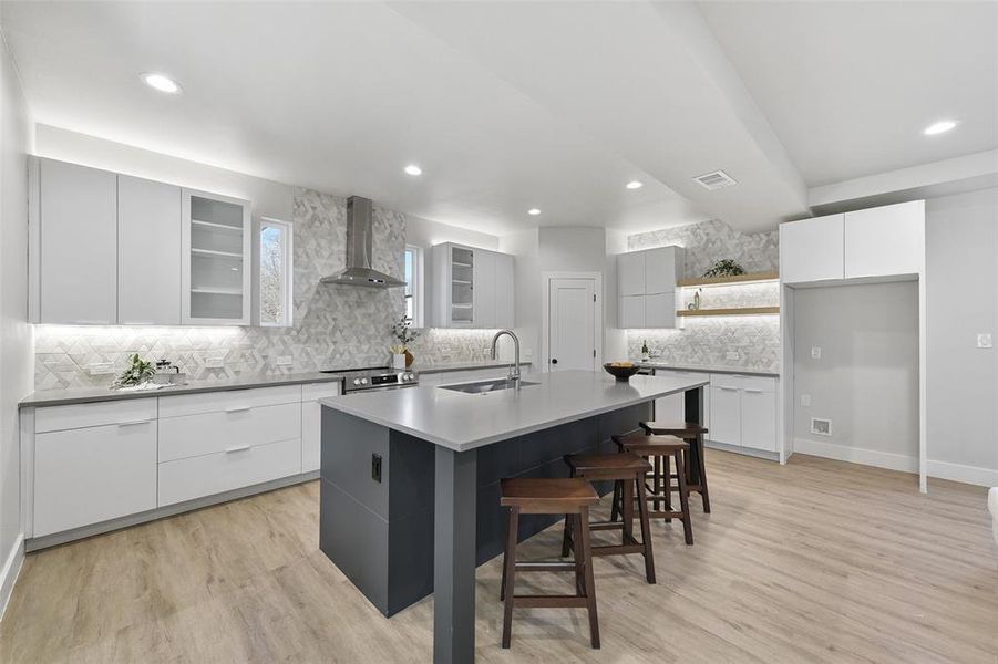 Kitchen featuring white cabinetry, a center island with sink, wall chimney exhaust hood, light hardwood / wood-style flooring, and sink