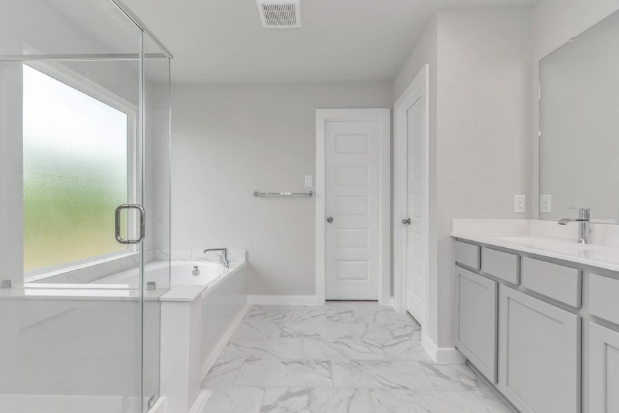 Escape to a spa-like oasis in this primary bathroom. Enjoy a walk-in shower with tile surround, a separate garden tub with custom detailing, and an elegant vanity featuring light countertops, modern hardware, and beautiful vanity lights. Experience luxury and relaxation in every detail. Sample photo of completed home with similar floor plan. Actual colors and selections may vary.