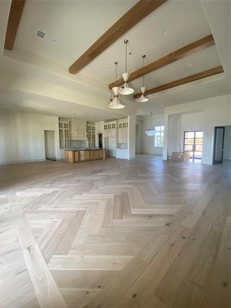 Empty room with an inviting chandelier, beamed ceiling, and light parquet floors