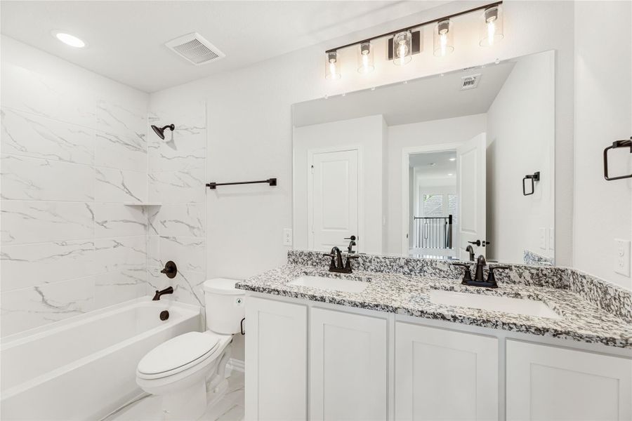 Bathroom with double sink vanity, granite countertop, white cabinets, and tub-shower with marble tile surround