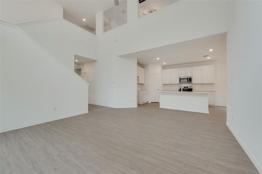 Unfurnished living room with light wood-type flooring and a towering ceiling