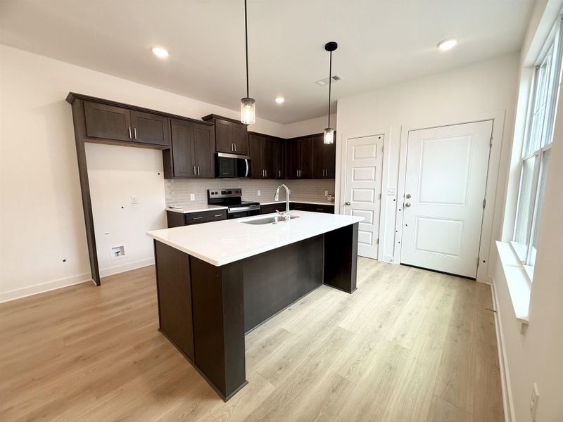 Kitchen with stainless steel appliances, a sink, dark brown cabinetry, light countertops, and backsplash Kitchen with stainless steel appliances, a sink, dark brown cabinetry, light countertops, and backsplash