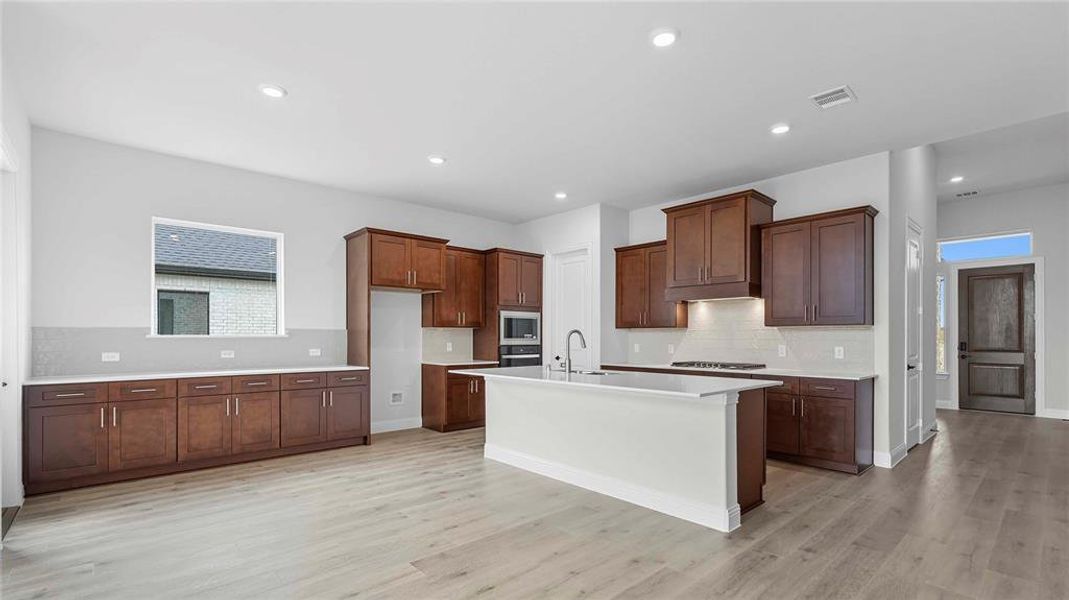 Open-concept kitchen featuring an expansive center island, extensive cabinetry with dark wood finishes, light-toned countertops, and wood-finish flooring