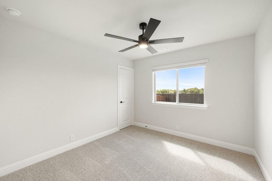 Empty bedroom with carpet flooring, black ceiling fan, white walls, and a single window with backyard view.