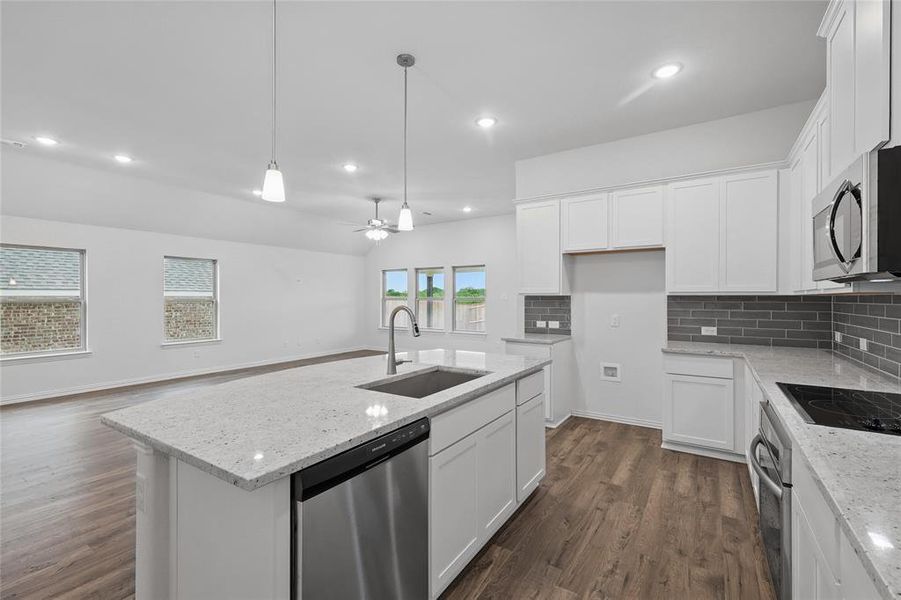 Kitchen with dark wood-type flooring, a sink, decorative backsplash, and appliances with stainless steel finishes Kitchen with dark wood-type flooring, a sink, decorative backsplash, and appliances with stainless steel finishes