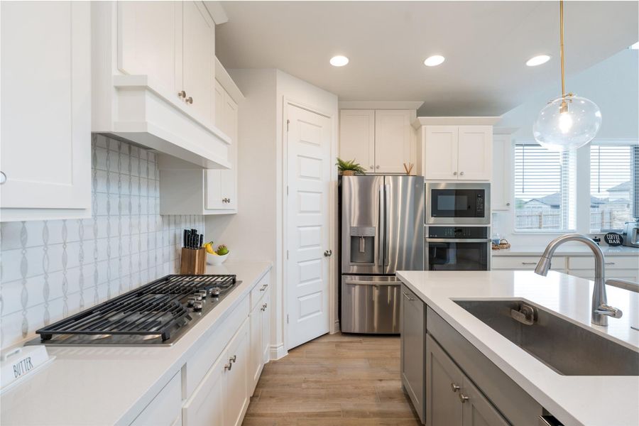 Two tone kitchen featuring stainless steel appliances, two tone color scheme, light wood-style flooring, decorative light fixtures, and decorative backsplash