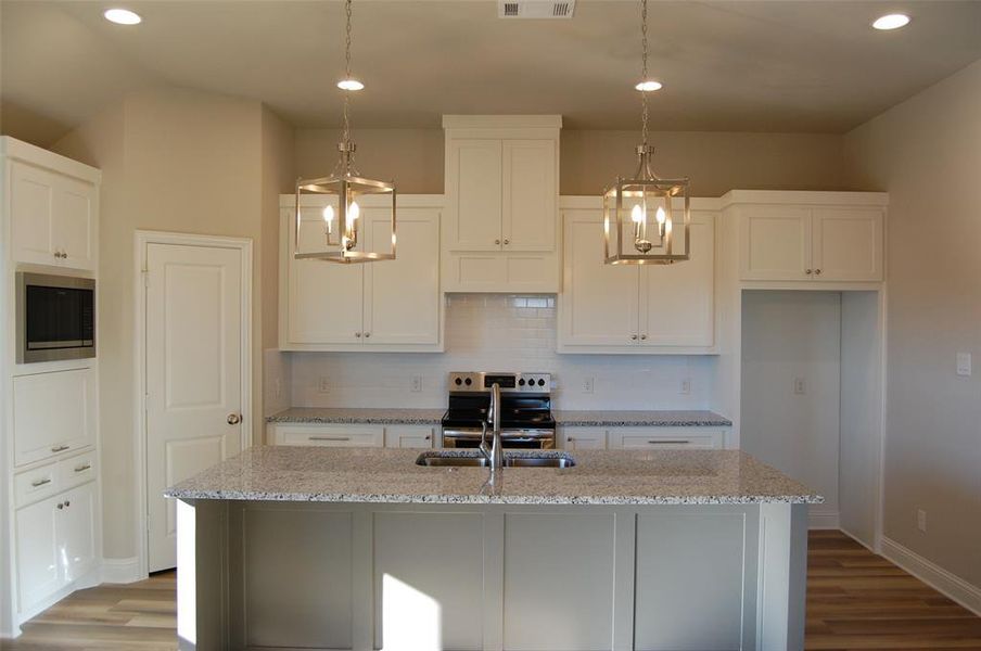 Kitchen featuring dark hardwood / wood-style floors, decorative light fixtures, and a kitchen island with sink