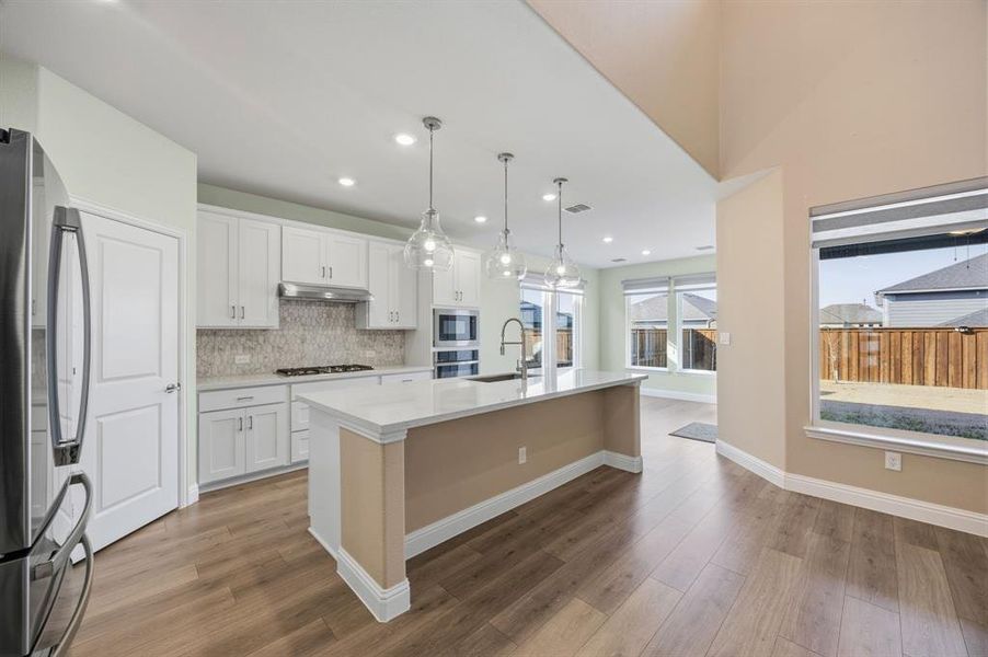 Kitchen featuring white cabinetry, a center island with sink, decorative light fixtures, and stainless steel appliances. Gas stovetop