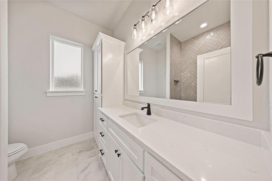 Full bath with vanity, baseboards, toilet, marble look tile flooring, and a tile shower Full bath with vanity, baseboards, toilet, marble look tile flooring, and a tile shower