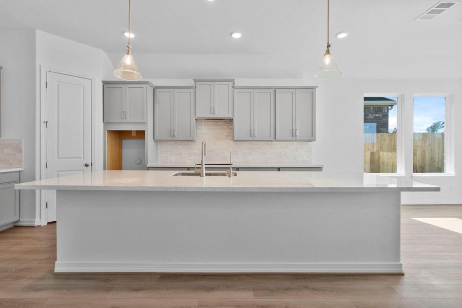 This light and bright kitchen features a large quartz island, gray cabinets, a large sink overlooking your family room, recessed lighting, and beautiful backsplash.