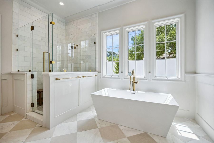 The spa-inspired primary bath showcases timeless finishes, featuring marble tile surround and elegant fixtures. A freestanding soaking tub is perfectly positioned beneath a wall of windows, while the oversized walk-in shower offers frameless glass enclosure and gorgeous tilework to the ceiling.