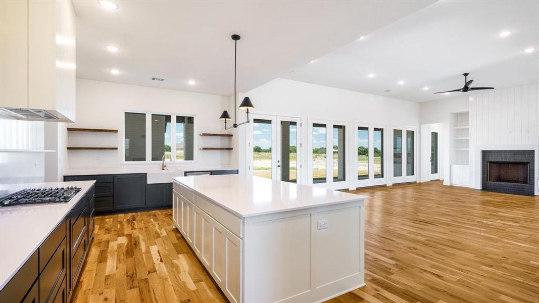 Kitchen featuring a center island, white cabinetry, light wood-type flooring, a large fireplace, and ceiling fan