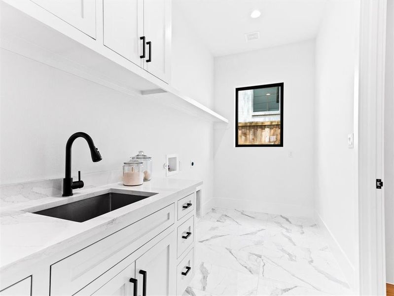 Kitchen with white cabinets, sink, light stone countertops, and light tile floors