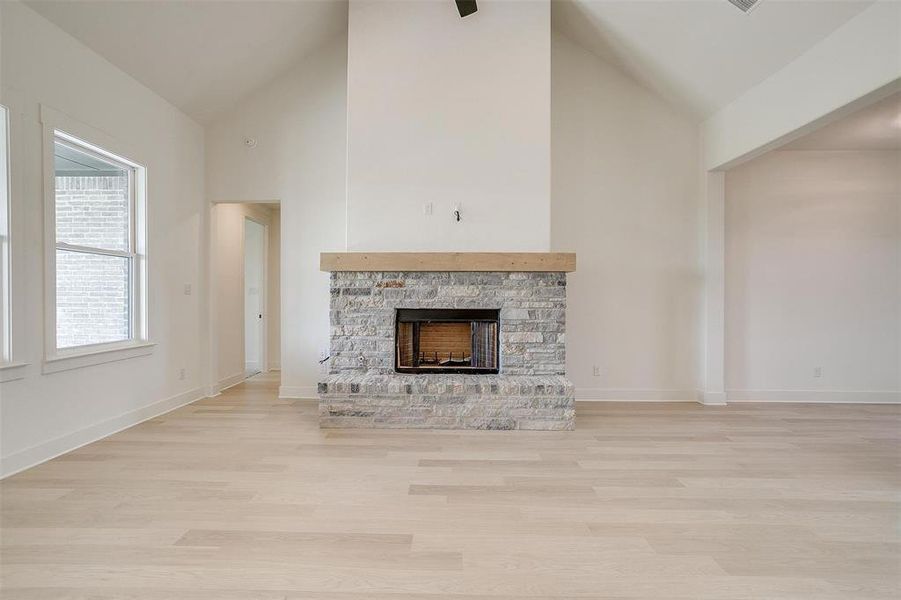 Unfurnished living room featuring light hardwood / wood-style flooring, a stone fireplace, and high vaulted ceiling