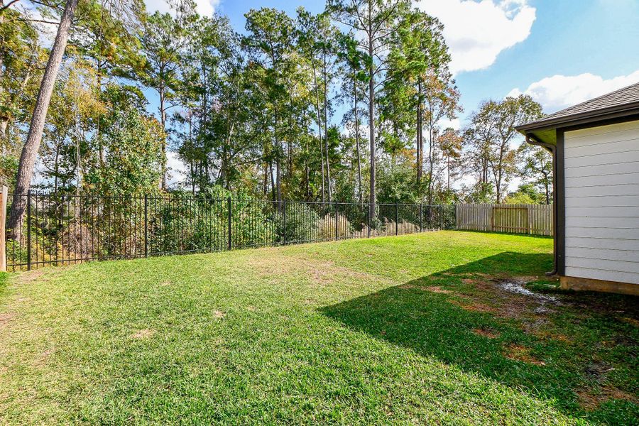 Spacious backyard bordered by a wrought iron and wooden fence and surrounded by mature trees, offering privacy and a peaceful view. Spacious backyard bordered by a wrought iron and wooden fence and surrounded by mature trees, offering privacy and a peaceful view.