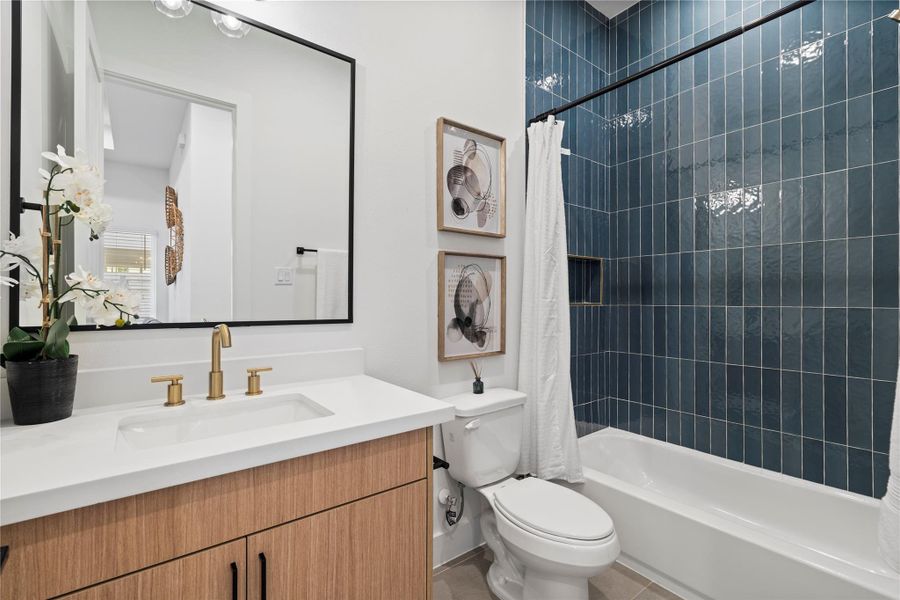 This secondary bathroom features lighter designer tilework paired with European-style white oak cabinetry, white quartz countertops, and champagne bronze Delta fixtures—creating a bright, sophisticated space that complements the home's refined finishes.