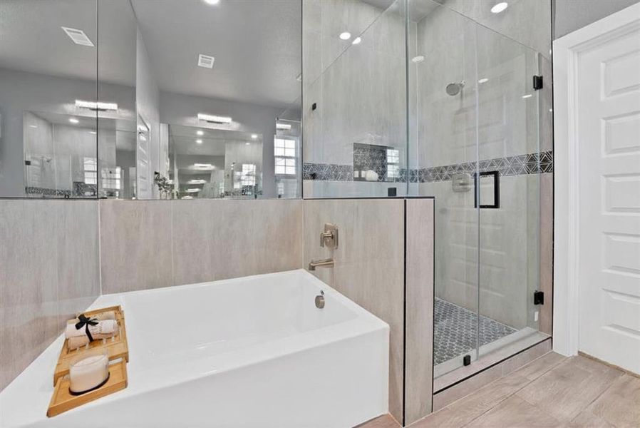 Freestanding soaking tub alongside a frameless glass shower with mosaic tile accents