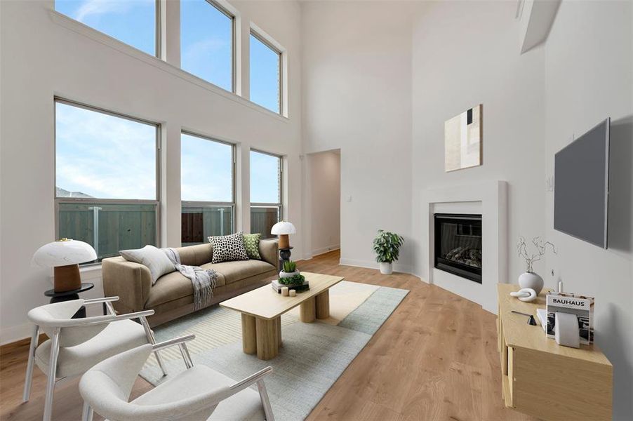 Living room with a glass covered fireplace, light wood-style floors, healthy amount of natural light, and a high ceiling