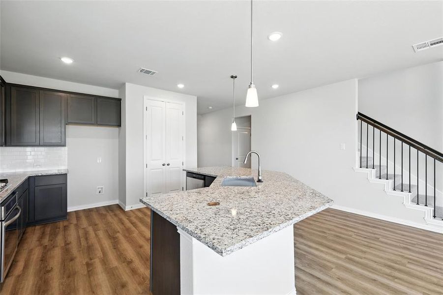 Kitchen with wood finished floors, light stone countertops, a center island with sink, recessed lighting, and backsplash Kitchen with wood finished floors, light stone countertops, a center island with sink, recessed lighting, and backsplash