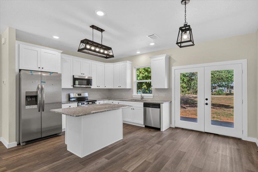 Double glass doors open to the outdoors from this kitchen with stone counters. Double glass doors open to the outdoors from this kitchen with stone counters.
