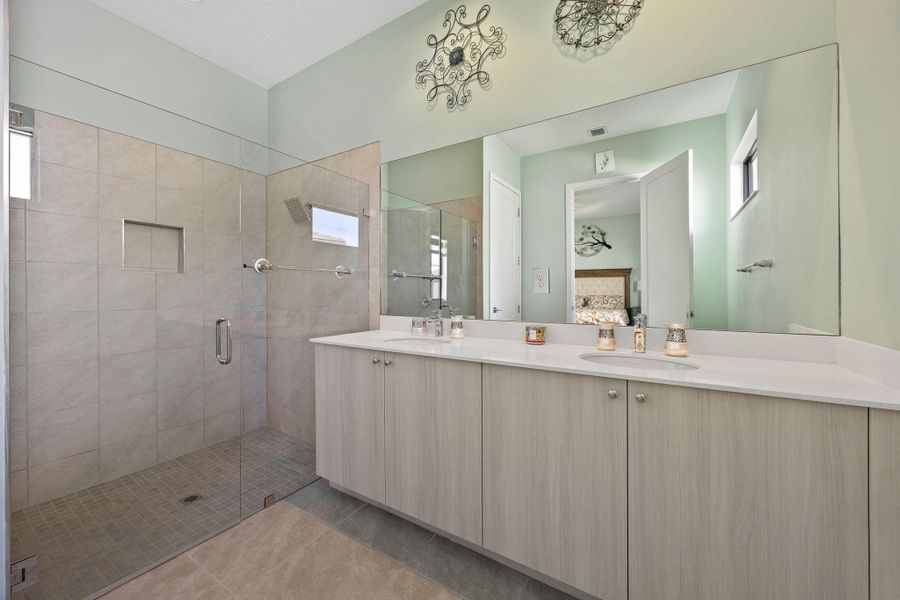 Ensuite bathroom with double vanity, a stall shower, plenty of natural light, and light tile patterned flooring