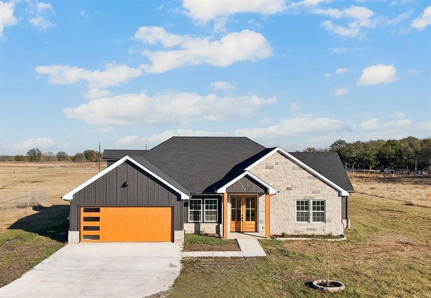 View of front facade featuring roof with shingles, a front yard, driveway, a garage, and stone siding