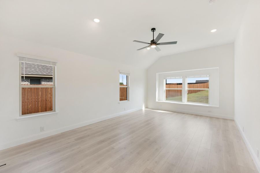 Empty living room with vaulted ceiling, ceiling fan, light wood floors, and three windows