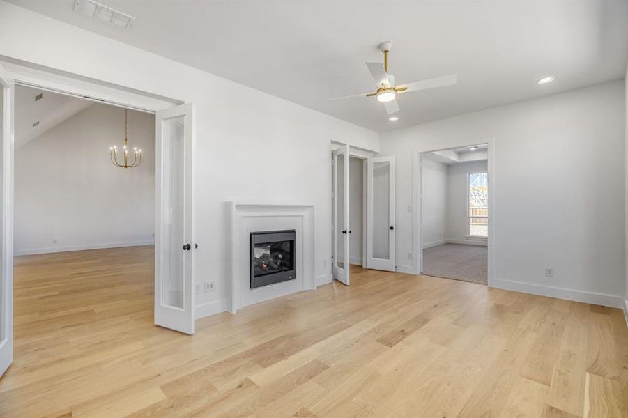 Unfurnished living room featuring a glass covered fireplace, light wood finished floors, ceiling fan, and a chandelier