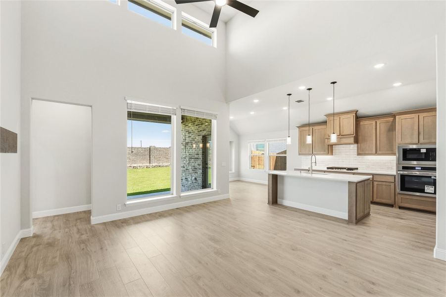 Open-concept living area with high ceilings, wood-look floors, and kitchen with island and stainless appliances