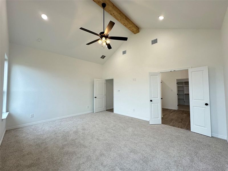 Unfurnished bedroom with a ceiling fan, high vaulted ceiling, carpet flooring, beamed ceiling, and a spacious closet