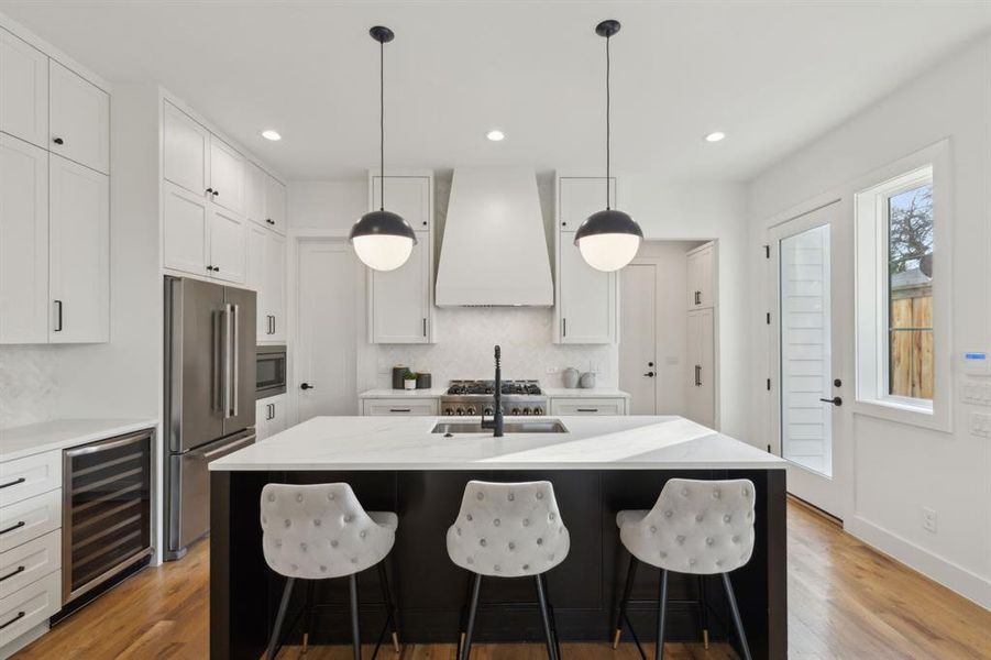 Kitchen featuring appliances with stainless steel finishes, white cabinetry, a center island with sink, and custom range hood