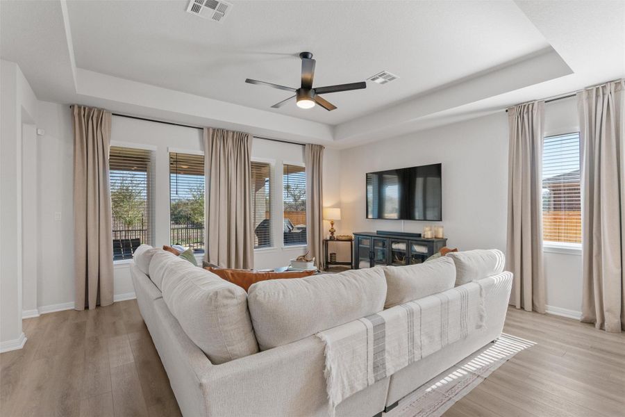 Living room featuring a ceiling fan, a raised ceiling, and light wood-style floors