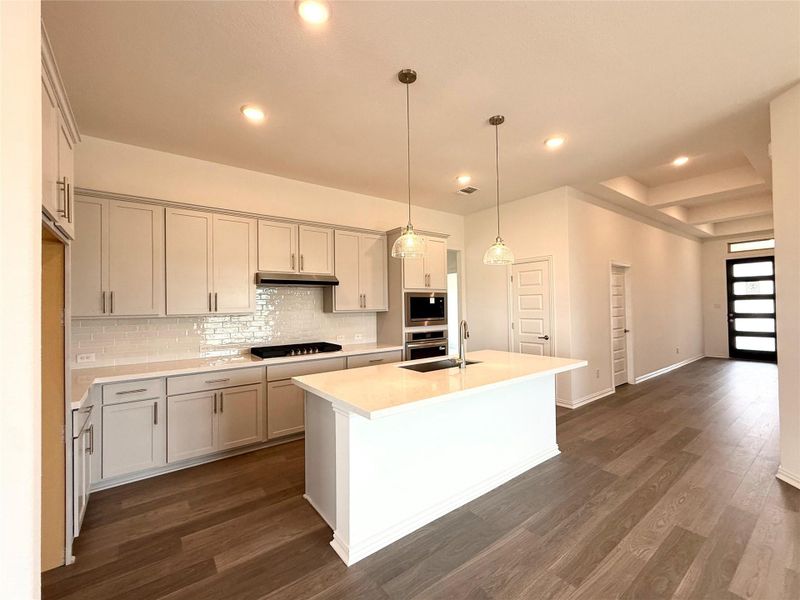 Kitchen with decorative backsplash, light countertops, dark wood-style flooring, a center island with sink, and recessed lighting Kitchen with decorative backsplash, light countertops, dark wood-style flooring, a center island with sink, and recessed lighting