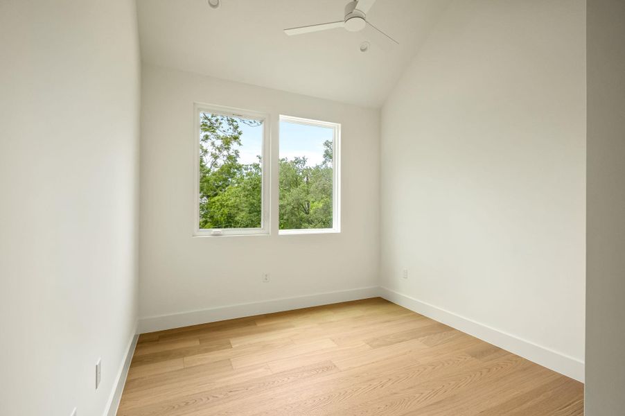 Hardwood floors and a pitched ceiling create a cozy, well-lit bedroom space.