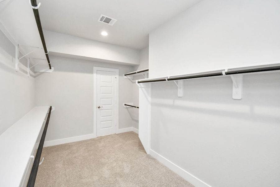 Walk-in closet that epitomizes luxury and practicality. This generously sized space features built-in shelving, offering abundant room for impeccable organization. High ceilings and recessed lighting create a bright and welcoming ambiance. Sample photo of completed home with similar floor plan. Actual colors and selections may vary.