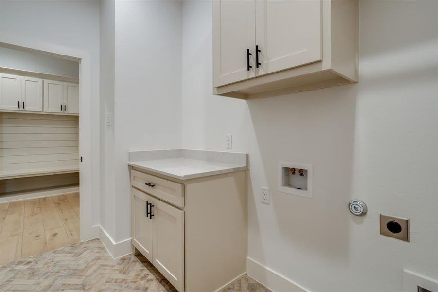 Laundry area with parquet floors, hookup for a washing machine, hookup for an electric dryer, and cabinet space