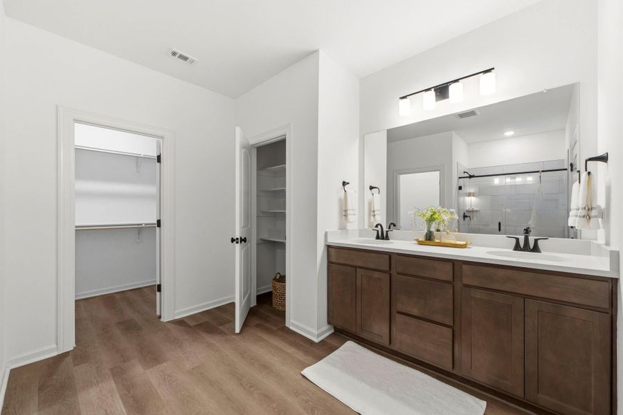 Spa-like primary bath with dual vanities, an oversized walk-in shower, linen storage, and a spacious walk-in closet.