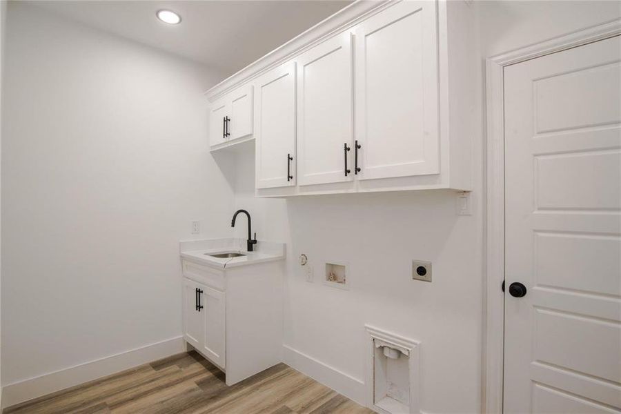 Clothes washing area with cabinets, light wood-type flooring, sink, and hookup for an electric dryer