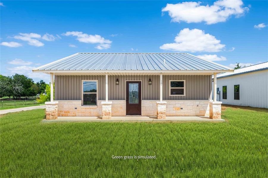 View of front facade featuring board and batten siding, covered porch, stone siding, and a front yard