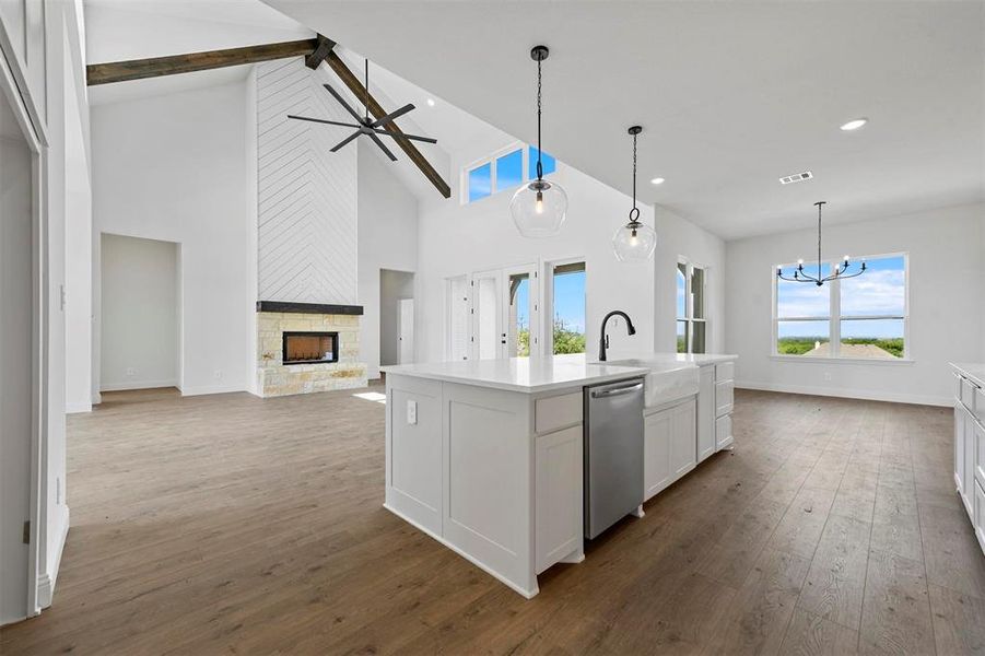 Kitchen with a stone fireplace, hardwood / wood-style floors, stainless steel dishwasher, beamed ceiling, and white cabinetry