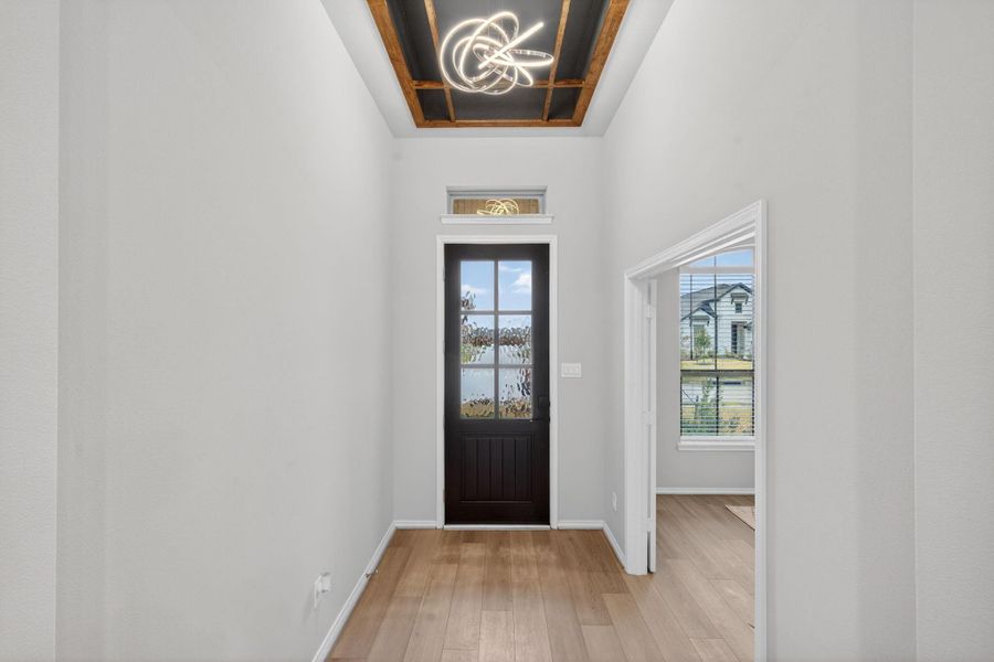 This entryway features a modern chandelier and high ceilings with an accent feature, leading to a dark front door with glass panels. Natural light filters in, complementing the light wood flooring and neutral walls, creating an inviting space. This entryway features a modern chandelier and high ceilings with an accent feature, leading to a dark front door with glass panels. Natural light filters in, complementing the light wood flooring and neutral walls, creating an inviting space.