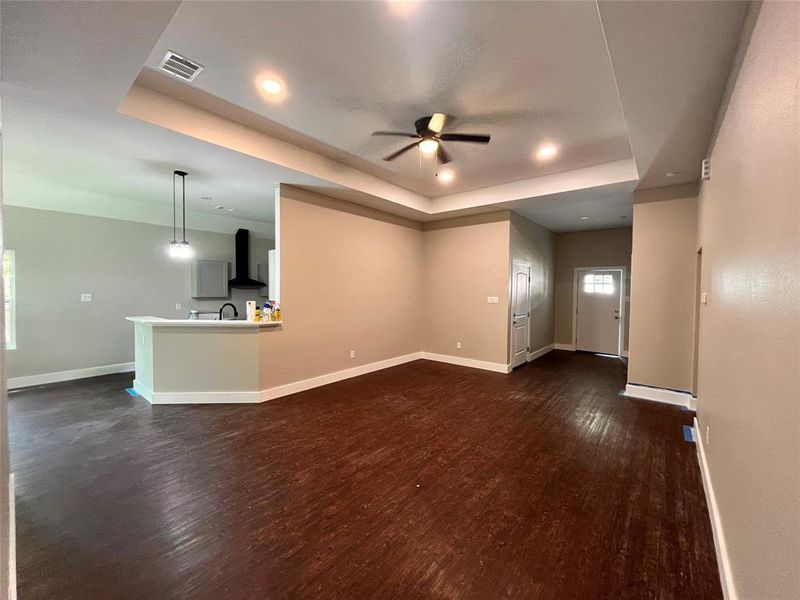 Unfurnished living room featuring a raised ceiling, dark wood-type flooring, and ceiling fan