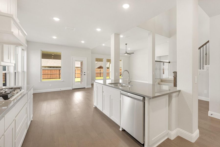 Kitchen with white island, stainless steel sink and dishwasher, open to living area with hardwood floors