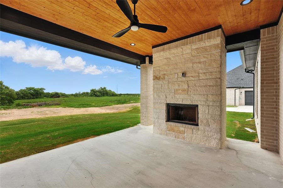 View of patio featuring an outdoor stone fireplace, a ceiling fan, and a view of rural / pastoral area