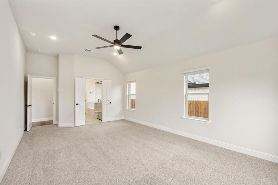 Empty bedroom with vaulted ceiling, ceiling fan, carpet flooring, and open doors to bathroom and closet Empty bedroom with vaulted ceiling, ceiling fan, carpet flooring, and open doors to bathroom and closet