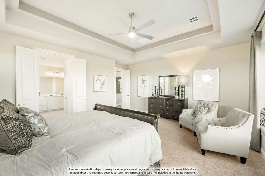 Master bedroom with tray ceiling, ceiling fan, sitting area, and ensuite bathroom visible through open door