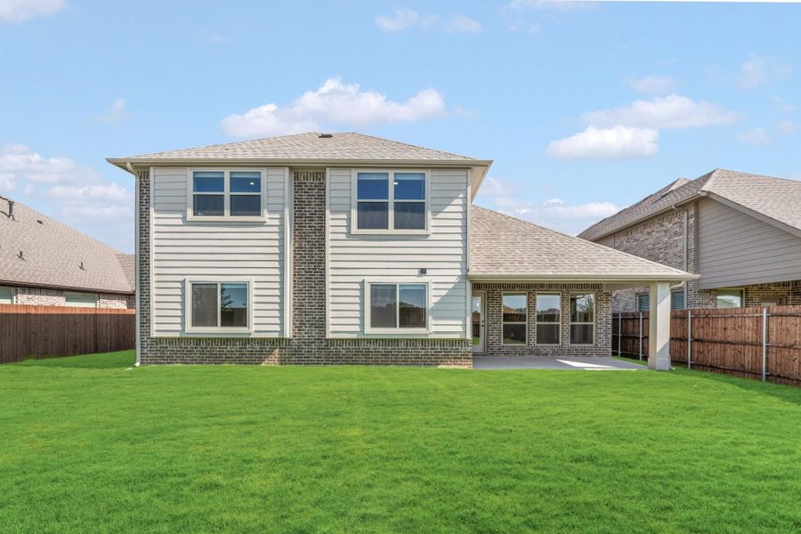 Two-story home rear exterior with brick and siding, covered patio, and fenced backyard with green lawn Two-story home rear exterior with brick and siding, covered patio, and fenced backyard with green lawn