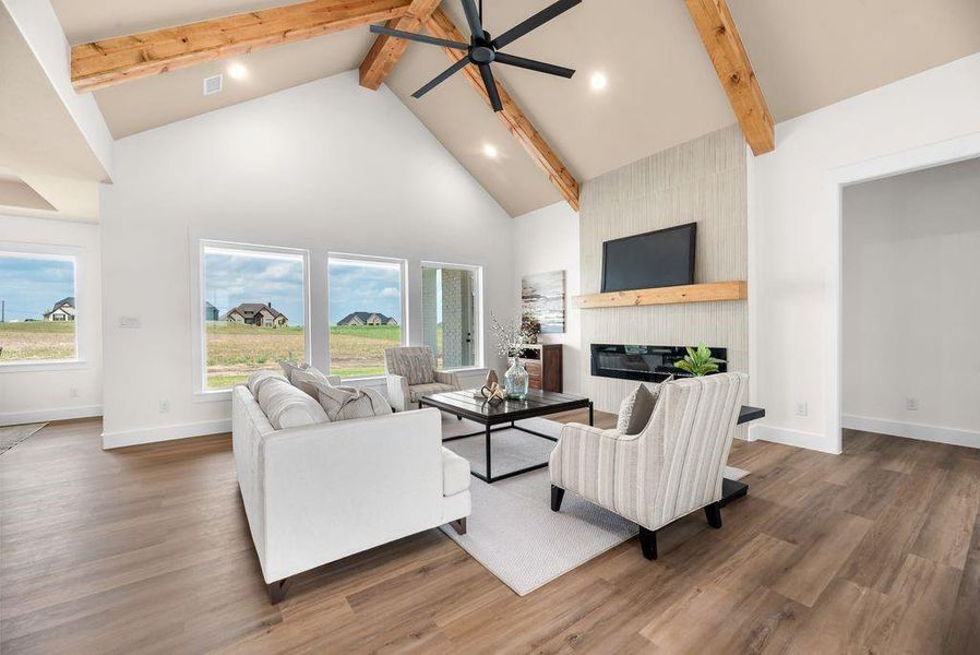 Living area featuring high vaulted ceiling, beam ceiling, a fireplace, wood finished floors, and a ceiling fan Living area featuring high vaulted ceiling, beam ceiling, a fireplace, wood finished floors, and a ceiling fan