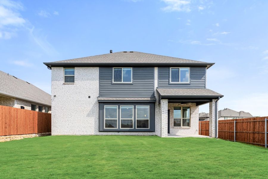 Two-story home rear view with white brick, gray siding, covered patio, and fenced backyard with green lawn